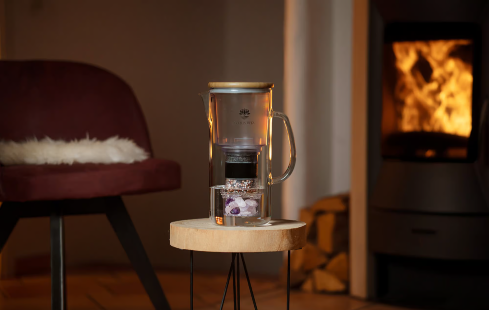A hand placing the Lotus Vita Crystal Holder, filled with rose quartz, amethyst, and rock crystal, into the ENYA glass water filter pitcher.